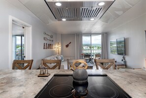 A modern kitchen with a black induction cooktop, wooden chairs, and a large window offering a city view.