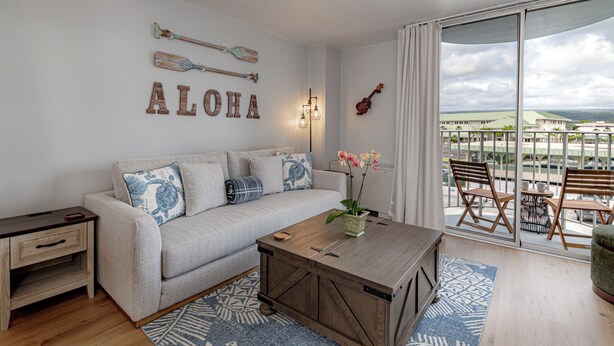 Una sala de estar con un sofá, una mesa de centro, una mesita auxiliar, una ventana con vistas y elementos decorativos en la pared.