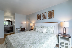 A bedroom with a large bed, a desk, a chair, a dresser, and wall art.
