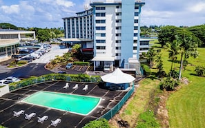 A hotel with a swimming pool, parking lot, and a large building with multiple floors.