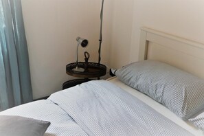 Een bed met strepen, een nachtkastje met een lamp en een raam met gordijnen.
