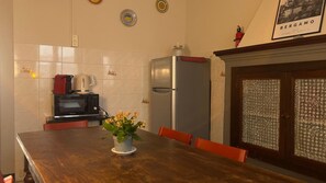 A kitchen with a microwave, kettle, and refrigerator. There is a dining table with chairs and a vase with flowers. - 'Papavero Piazza Delfino' Apartment with Balcony and Wi-Fi (Bergamo)