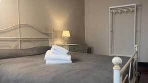Ein ordentlich bezogenes Bett mit einem gefalteten weißen Handtuch, ein Nachttisch mit einer Lampe und ein Kleiderschrank mit Spiegel.