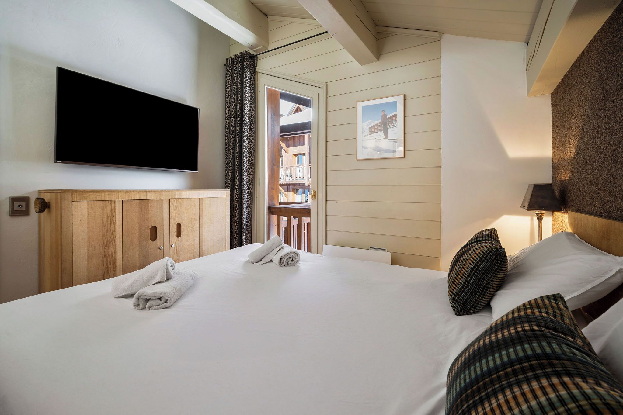 A hotel room with a bed, a television mounted on the wall, a door leading to a balcony, and a framed picture on the wall.