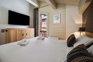 A hotel room with a bed, a television mounted on the wall, a door leading to a balcony, and a framed picture on the wall.