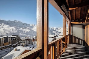 A wooden balcony with a view of snow-covered mountains and buildings.