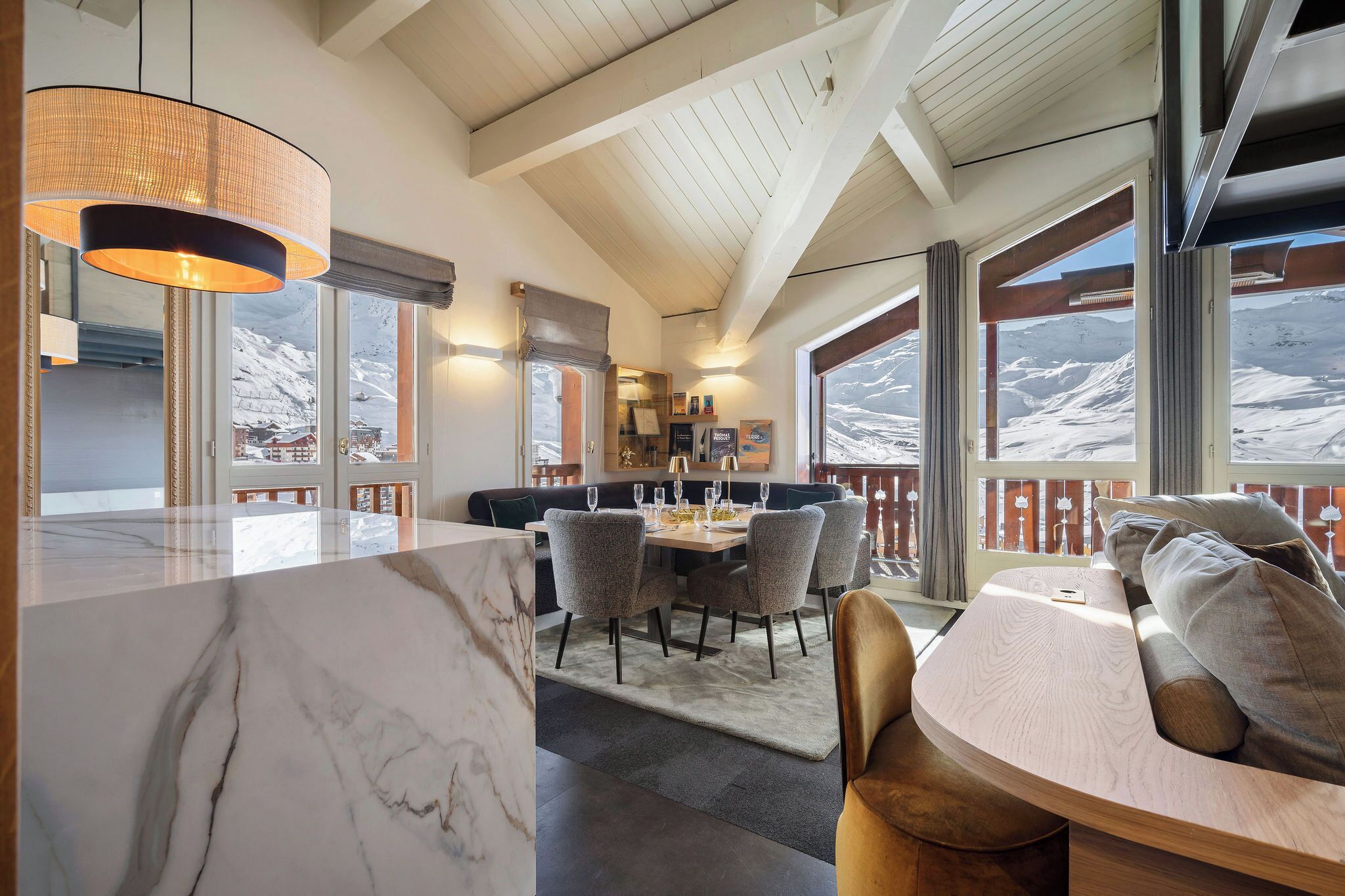 A modern interior with a marble countertop, dining area with chairs, a wooden ceiling, and large windows with a snowy view.