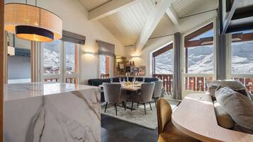 A modern interior with a marble countertop, dining area with chairs, a wooden ceiling, and large windows with a snowy view.