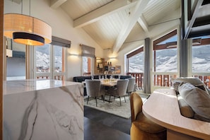 A modern interior with a marble countertop, dining area with chairs, a wooden ceiling, and large windows with a snowy view.