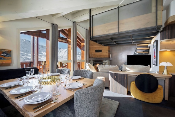 A modern dining area with a wooden table set for a meal, a sofa, and a kitchen area with a fireplace.