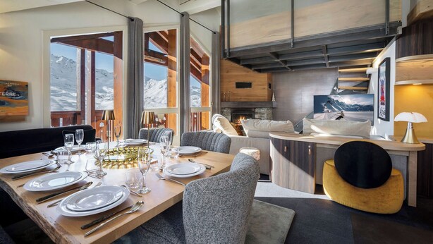 Un espace de repas moderne avec une table en bois dressée pour le repas, un canapé et une cheminée.