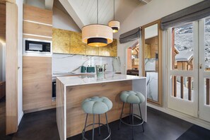 A modern kitchen with a central island, bar stools, a microwave, and a large window with a view of a snowy landscape.