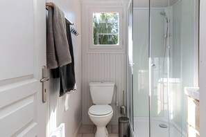 Ett litet badrum med en toalett, en dusch med glasväggar och ett fönster ovanför toaletten.