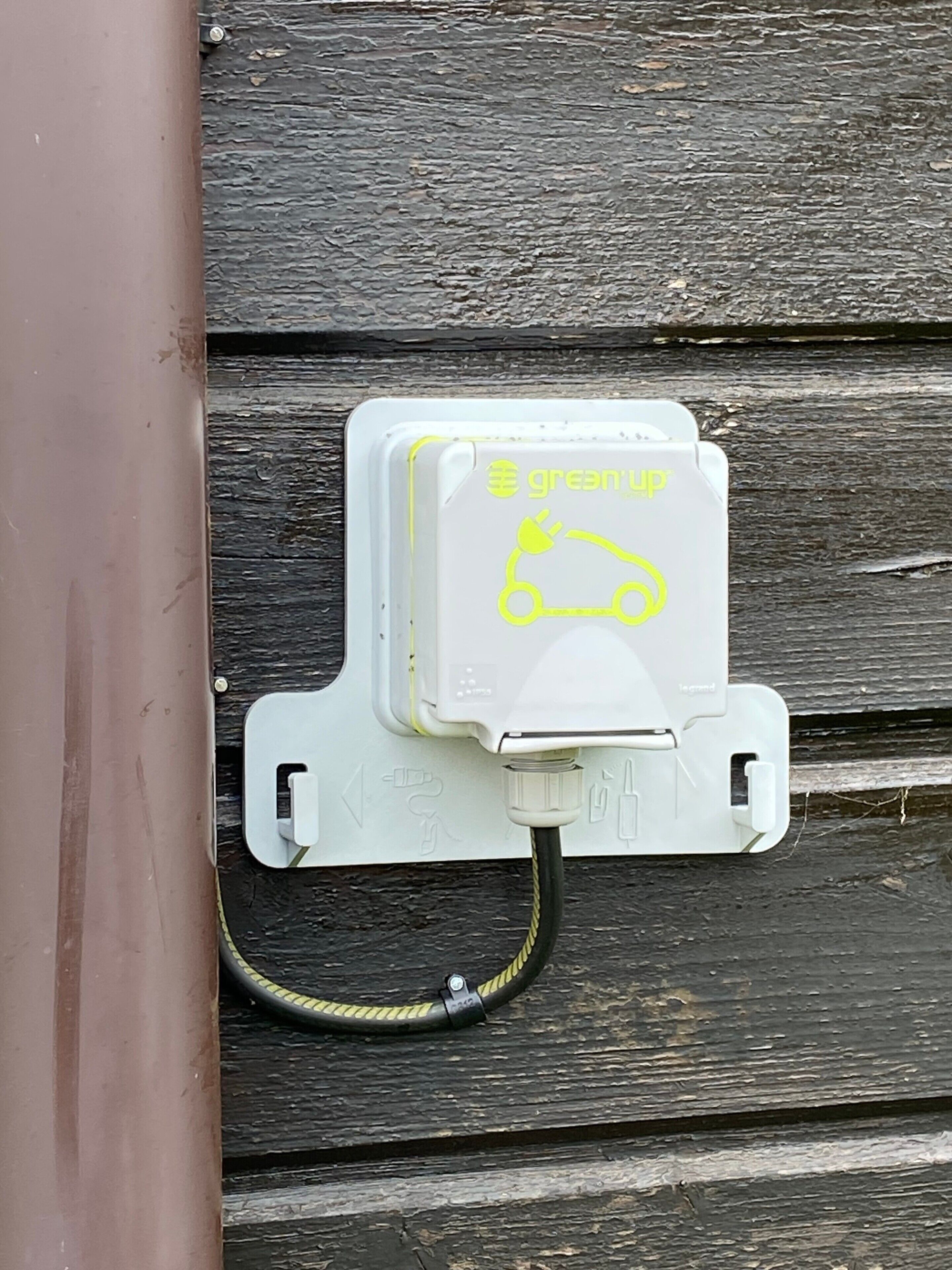 Een witte elektrische doos met stekker en kabel, bevestigd aan een houten wand.
