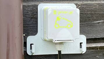 Een witte elektrische doos met stekker en kabel, bevestigd aan een houten wand.