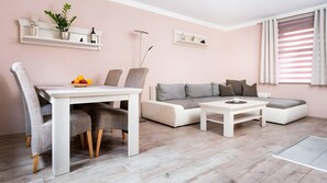 Una sala de estar moderna con un sofá blanco, sillones grises, una mesa de comedor con sillas y una pequeña mesa de centro.