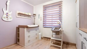 A child's bedroom with a crib, a changing table, a wardrobe, and a guitar on the wall.