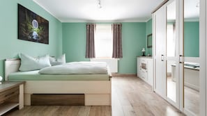 A bedroom with a bed, bedside table, wardrobe, and a window with curtains.