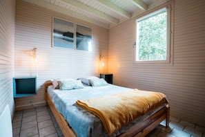 Une chambre à coucher avec un lit, deux lampes fixées au mur, une fenêtre et deux tableaux encadrés accrochés au mur.