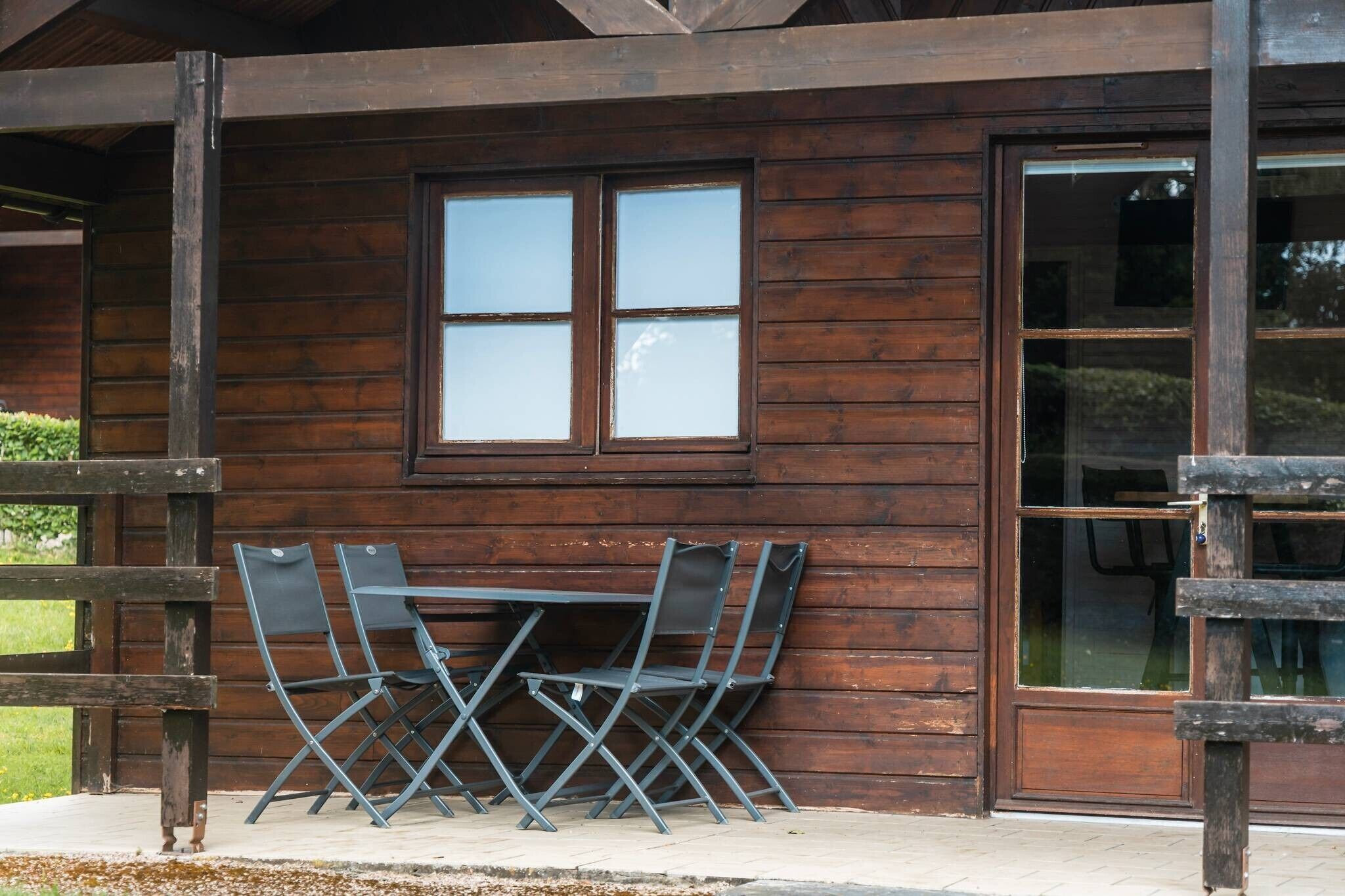 A wooden cabin with a table and chairs outside, a large window, and a door.