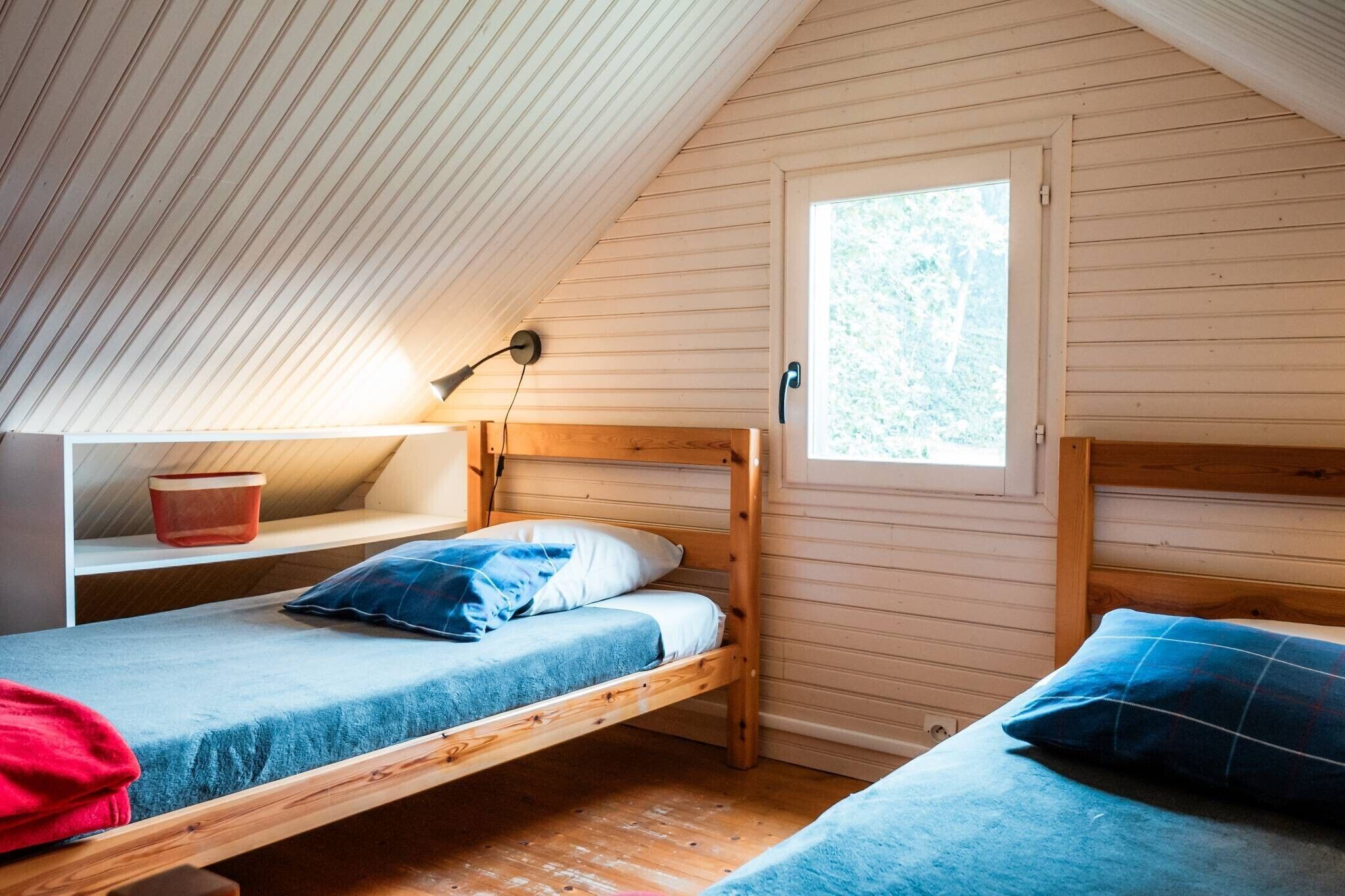 Une petite chambre mansardée, chaleureuse et accueillante, avec un plafond en pente, une fenêtre et deux lits superposés.