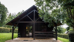 Eine Holzhütte mit überdachter Veranda, Grill und gepflegtem Rasen.