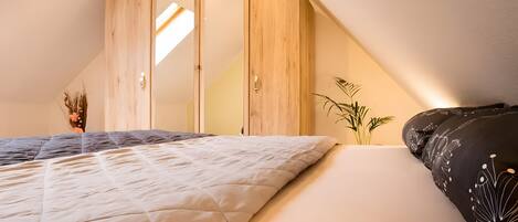 A bedroom with a bed, a wardrobe, a bedside plant, and a window.