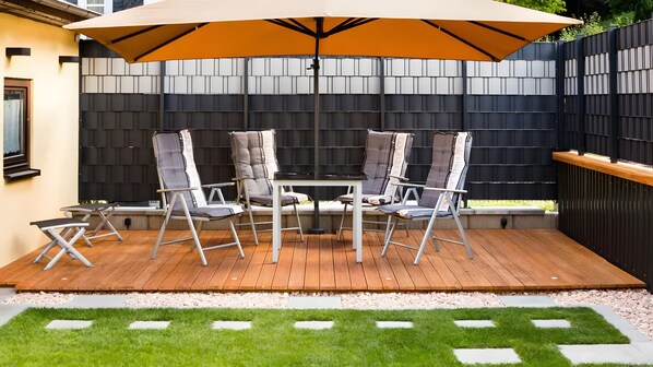 Eine Terrasse mit Tisch, Stühlen und einem Sonnenschirm, begrenzt durch einen schwarzen Zaun.