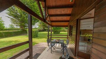 A covered patio with a table and chairs, a grill, and a view of a well-maintained garden.
