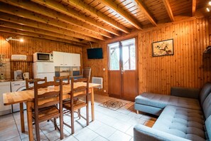 Un interior de madera con una mesa de comedor, sillas, un sofá, un televisor y electrodomésticos de cocina.
