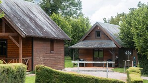 Two wooden cabins with pitched roofs, a covered outdoor seating area, and a well-maintained garden. - Chalet Pillette for 6 with shared pool, private terrace, and Wi-Fi (Livarot-Pays-d'Auge)
