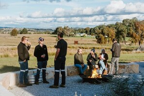 A group of people around a campfire in an outdoor setting with a rural landscape in the background. - 'Cascade' at Small Batch (Budgee Budgee)