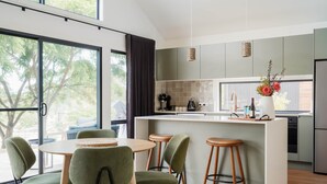 Een moderne keuken met een centraal eiland, barkrukken en een eettafel met stoelen.