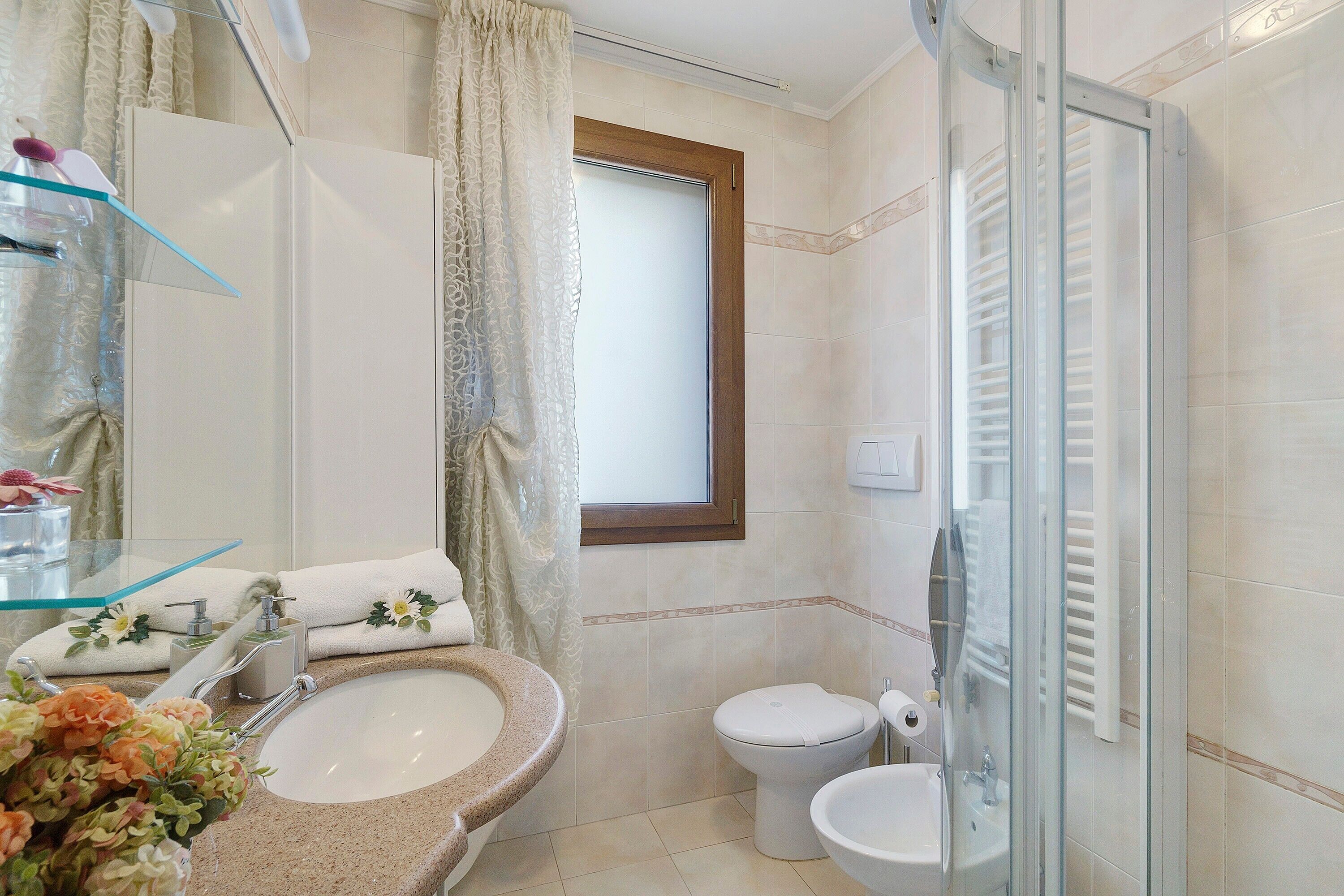 Un baño con cabina de ducha de vidrio, inodoro, lavamanos y ventana.