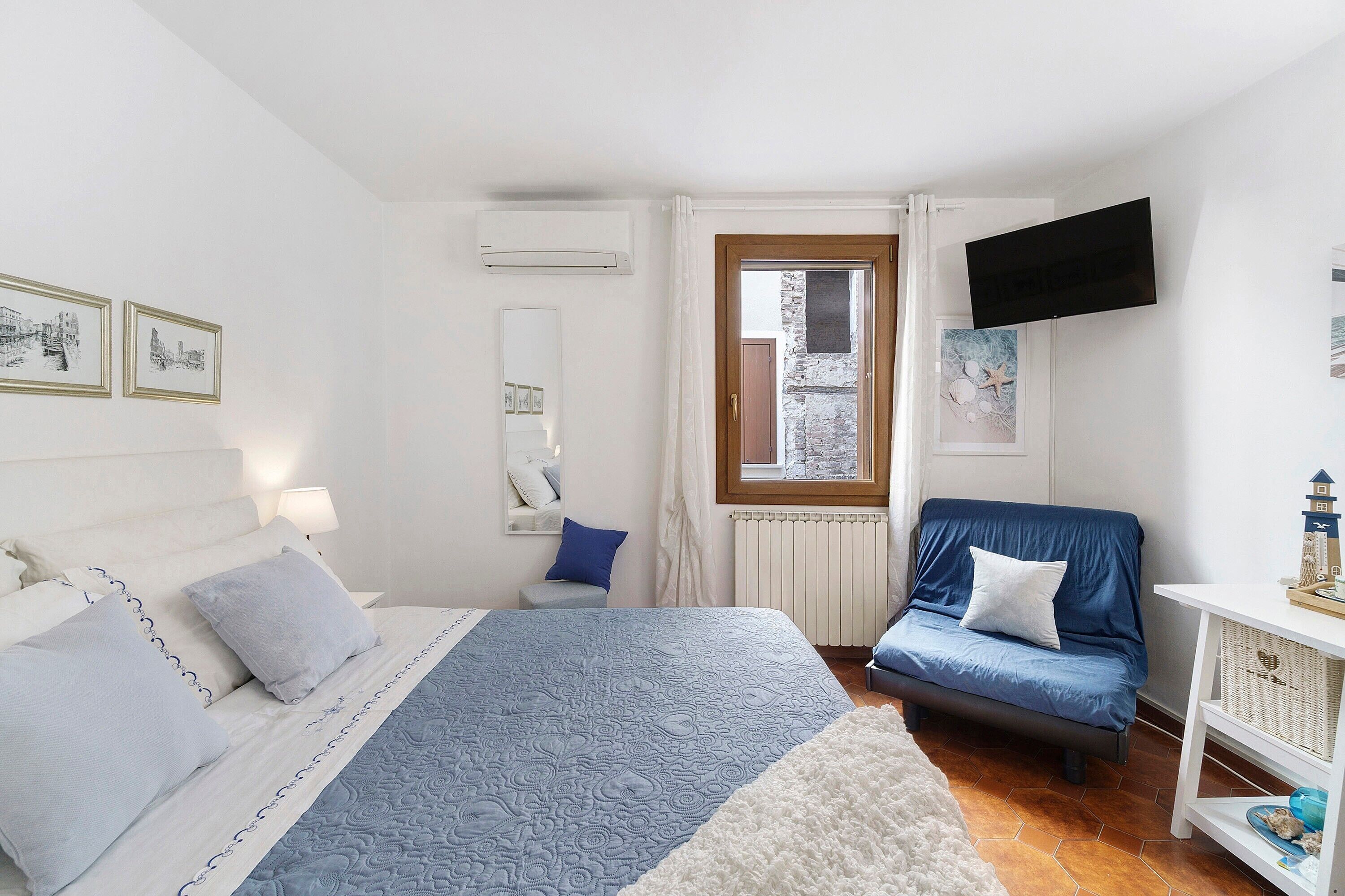 Quarto com cama, uma cadeira, televisão e janela.