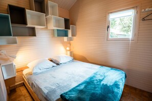 Un dormitorio con cama, mesita de noche, estantes en la pared, una ventana y una lámpara colgante.