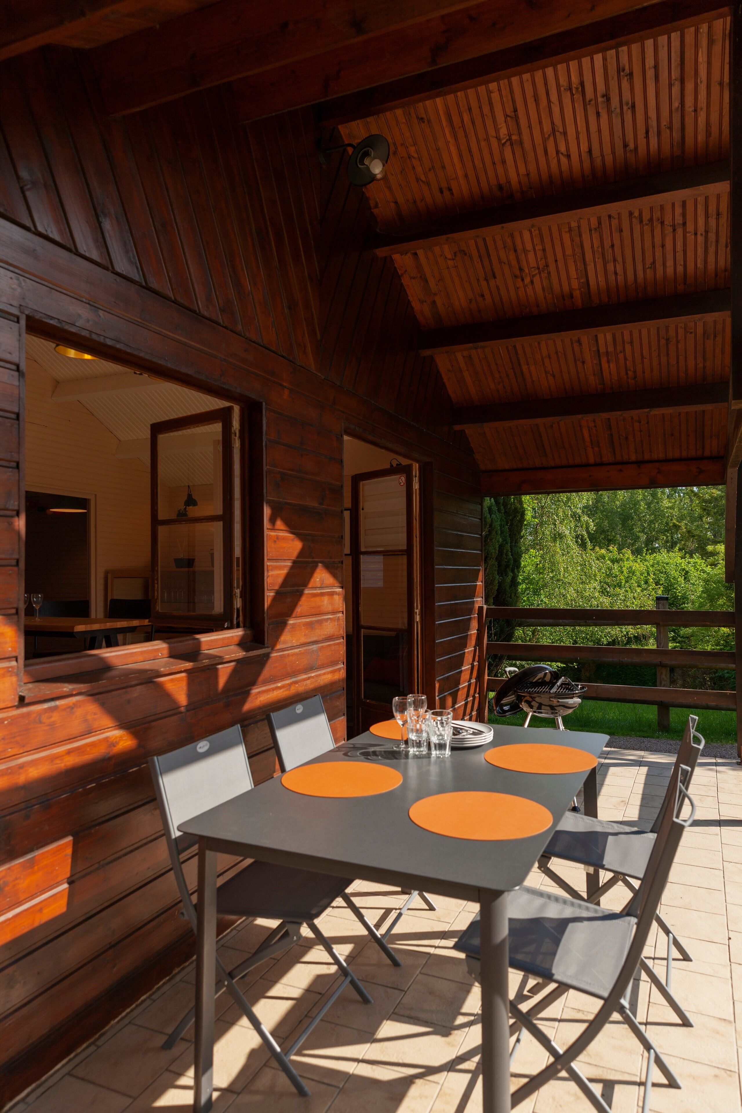 A wooden cabin with a dining area featuring a table and chairs, a view of the outdoors, and a window with a view of greenery.