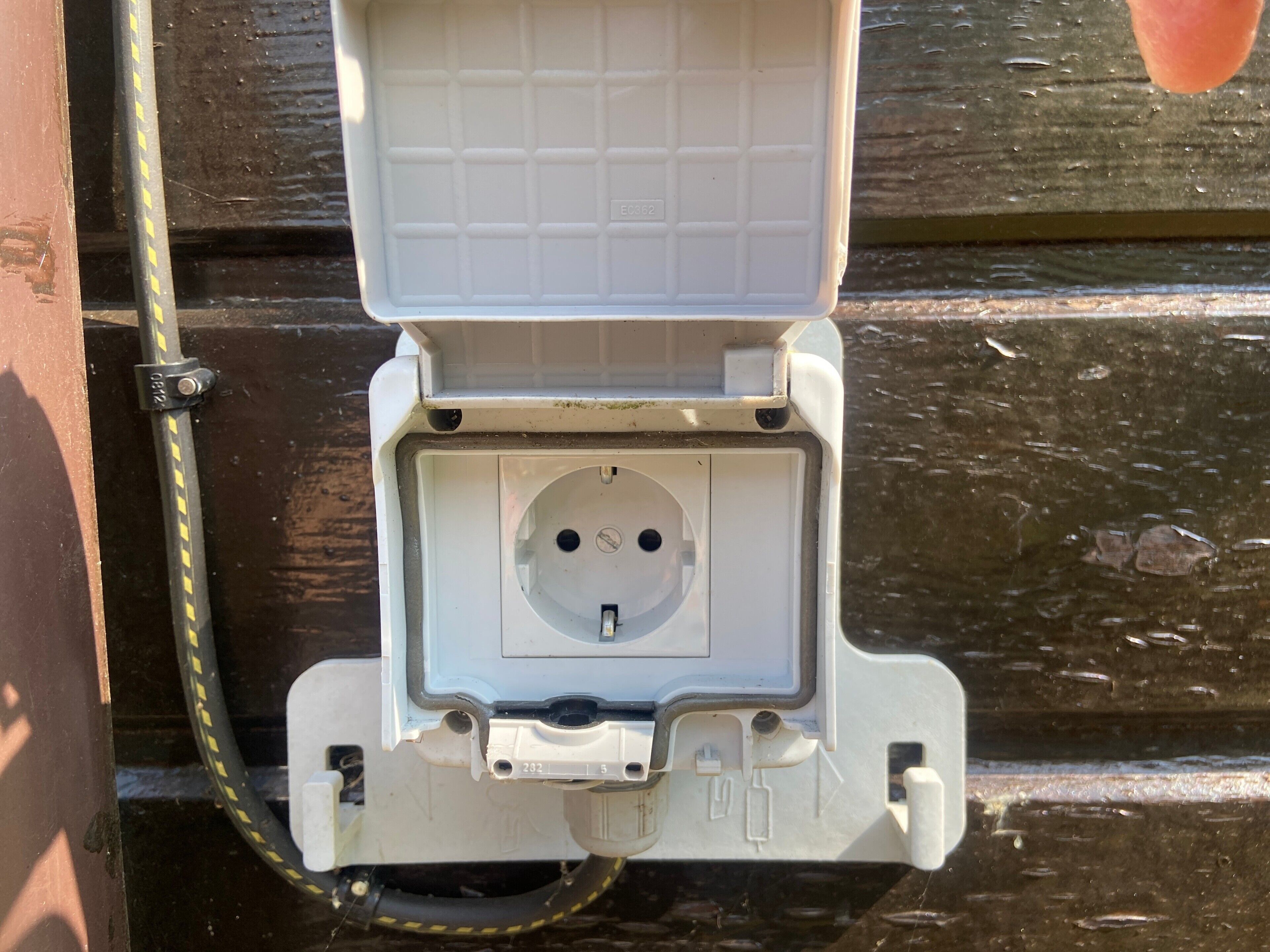 An electrical box with a cable connected to it, mounted on a wooden surface.
