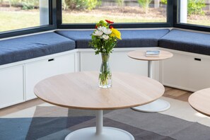 A seating area with a round table and a vase of flowers. - Villa Les Flots de la Torche — Luxury Designer Villa with Panoramic Sea View (Penmarch)