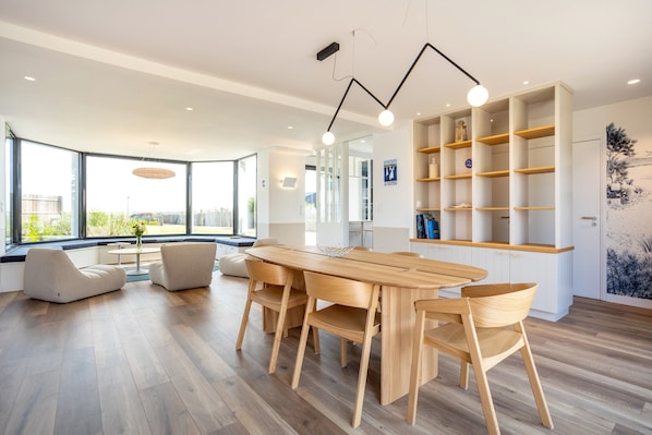 Une cuisine moderne avec une table et des chaises en bois, une bibliothèque intégrée et de grandes fenêtres donnant sur un paysage verdoyant.