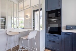 A modern kitchen with a white table and bar stools, a Bosch microwave, and a built-in oven. - Villa Les Flots de la Torche — Luxury Designer Villa with Panoramic Sea View (Penmarch)