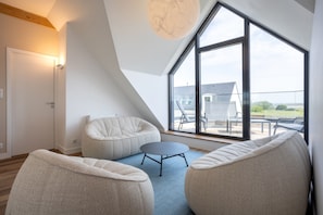 Une chambre de style loft moderne, dotée d’une grande lucarne, d’une table ronde et de deux fauteuils en forme de poire.