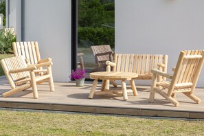 A patio with wooden chairs and a table, a potted plant, and a view of greenery through a glass door. - Villa Les Flots de la Torche — Luxury Designer Villa with Panoramic Sea View (Penmarch)