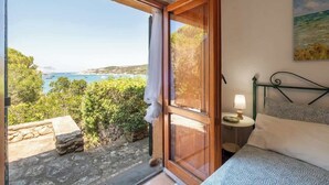 Ein Schlafzimmer mit Meerblick, einem Bett, einem Nachttisch und einem Fenster mit Vorhang.