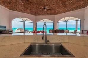 A modern bathroom with a marble sink, a ceiling fan, and large arched windows overlooking the ocean. - Cerquita del Mar – Beachfront, Rocky Point (Puerto Peñasco)