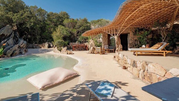 Ein Pool mit Holzterrasse, Liegestühlen und einer Steinmauer.