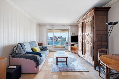 A living room with a sofa, a wooden table, a cabinet, and a view through a glass door.. ‘T2 Val Fleuri Near Beaches’ Apartment with Private Terrace