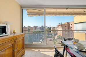 Un balcon donnant sur des immeubles, une table avec de la vaisselle et un four à micro-ondes posé sur un meuble.