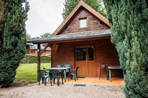 Una cabaña de madera con un patio, una mesa y sillas, y una puerta.
