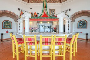 A restaurant with a central island, white columns, and red and yellow chairs. - Cerca del Mar – Beachfront, Sleeps 10, Rocky Point (Puerto Peñasco)